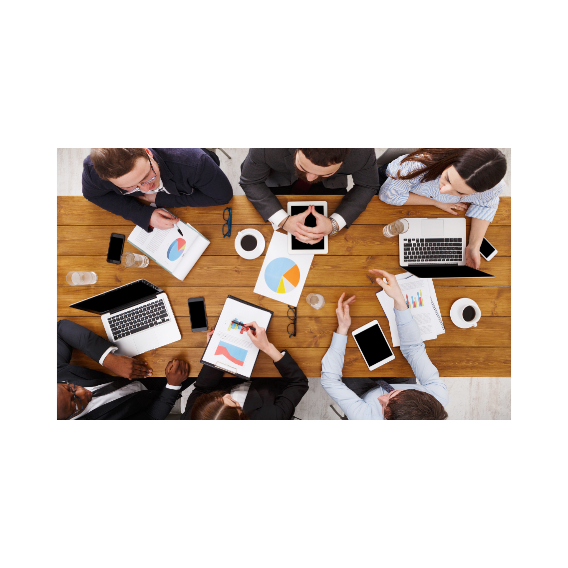 Top view of people sitting around a conference table with laptops and papers with charts and graphs